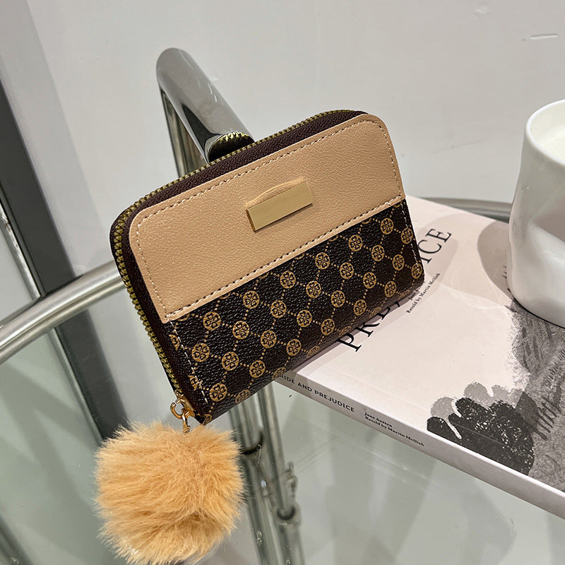 Beige and dark patterned short wallet with gold clasp and fuzzy pom-pom