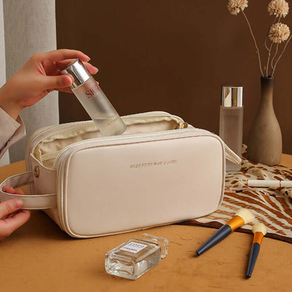 Cream cosmetic bag with double zippers, shown closed with a hand lifting the zipper