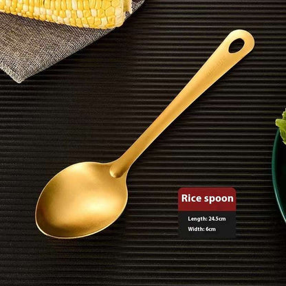 Gold rice spoon on a textured black surface with corn and a plant in the background