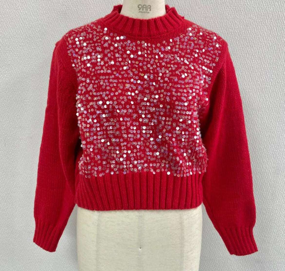 Red sweater with sequin pattern on a mannequin against a gray background