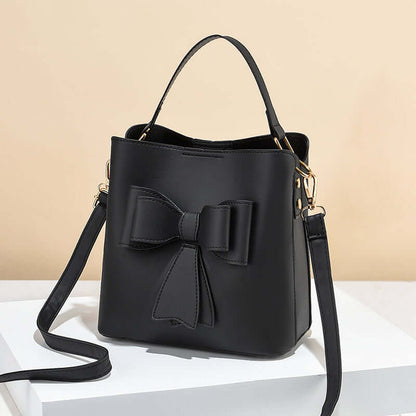Black bow bucket crossbody bag with gold-tone zippers and curved shoulder strap
