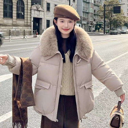 Person wearing a beige puffer jacket with fur collar on a city street.