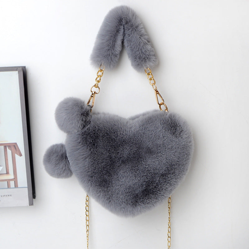 Heart-shaped plush handbag with pom-pom accents and gold chain strap, dark gray