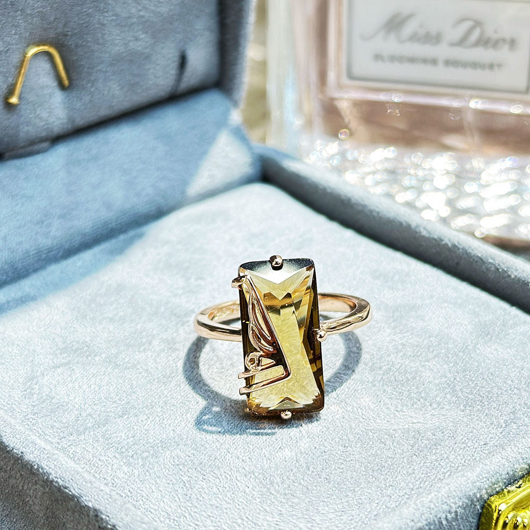Gold-tone rectangular gemstone ring on a blue velvet jewelry display
