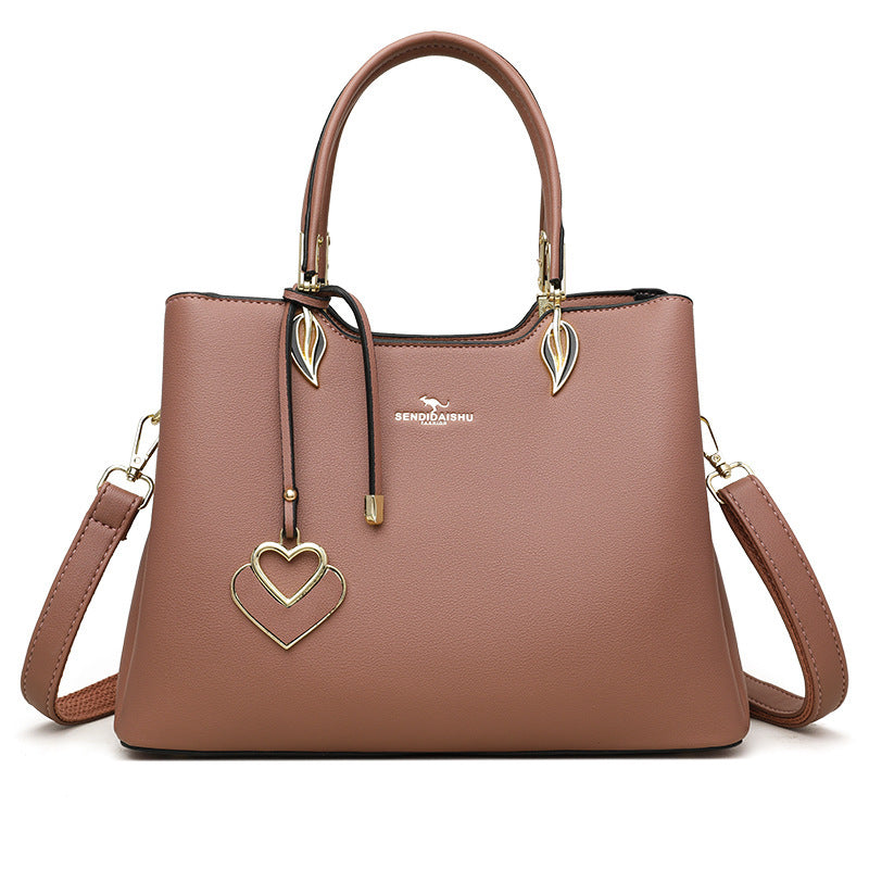 Women's shoulder bag in tan with top handles, heart charm, and crossbody strap