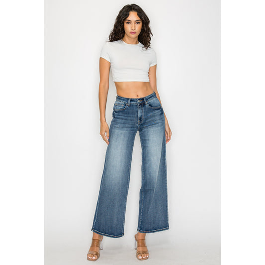A curvy model wearing dark blue high-waisted flare trousers with a wide-leg cut, styled with a tucked-in blouse to emphasize the waistline.