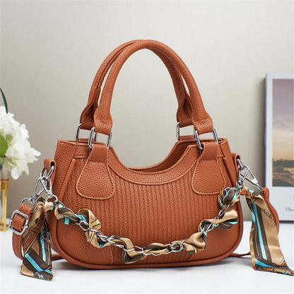 Rust orange braided chain crossbody handbag with top handles, textured fabric, side tabs.