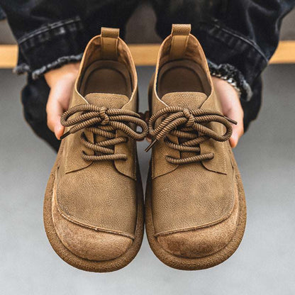 Pair of brown suede shoes held by a person against a neutral background