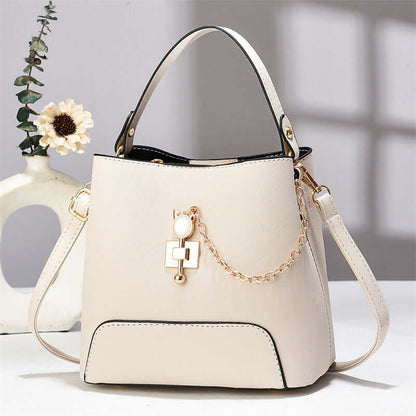 Light beige PU leather bucket bag with top handle, shoulder strap, and gold chain charm