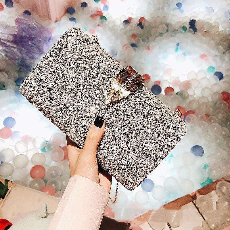 Black glitter evening bag clutch with leaf-shaped lock, held over a confetti backdrop