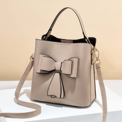 Beige bow bucket crossbody bag with bow applique and adjustable crossbody strap