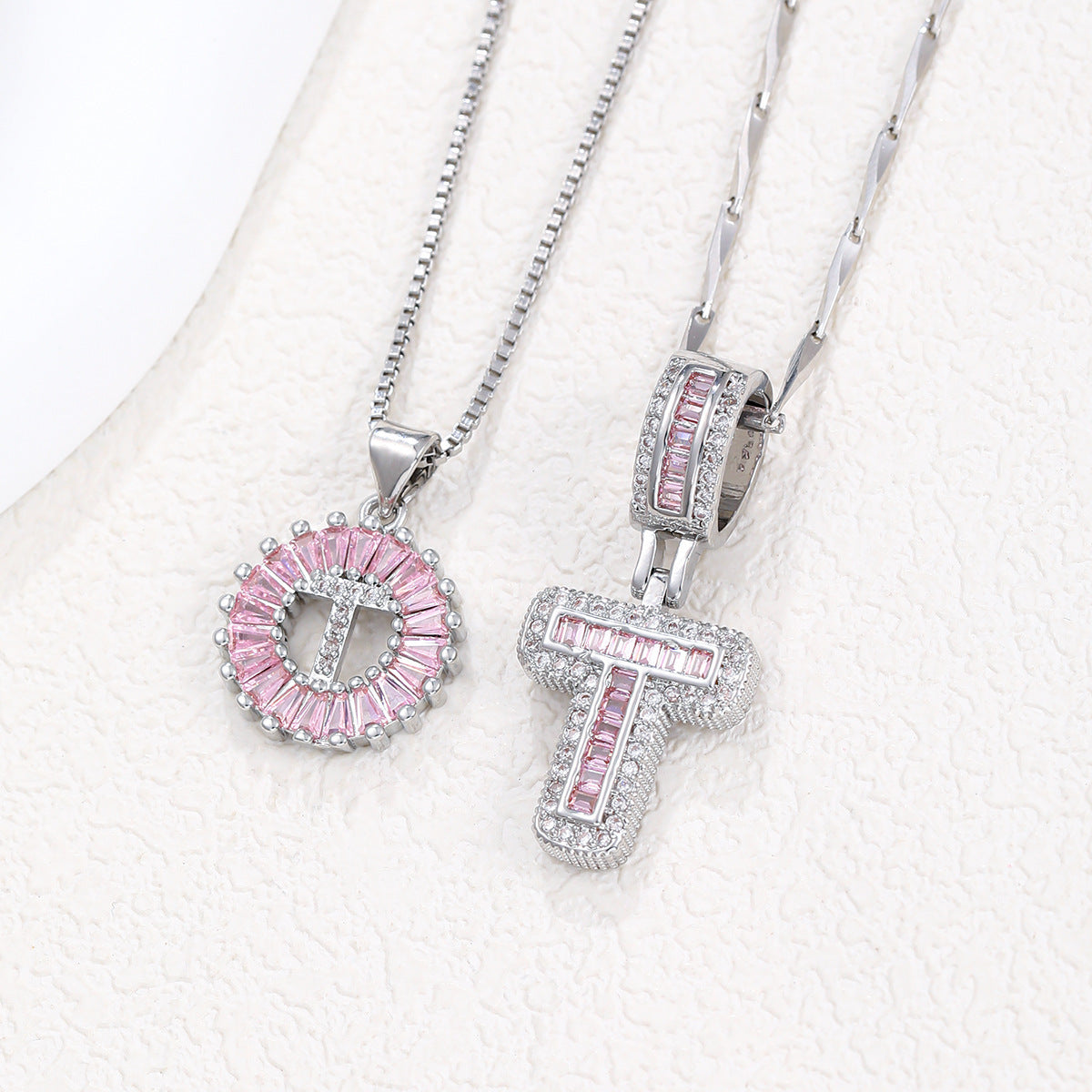 Silver-tone pendant necklace set with pink zircon rosette pendant and crossbar block letter pendant.