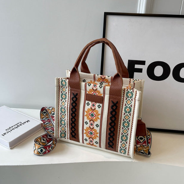 Hand-woven shoulder messenger bag with beige geometric print and brown leather handles on a desk