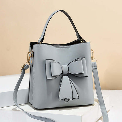 Light gray bow bucket crossbody bag with wide bow front and shoulder strap