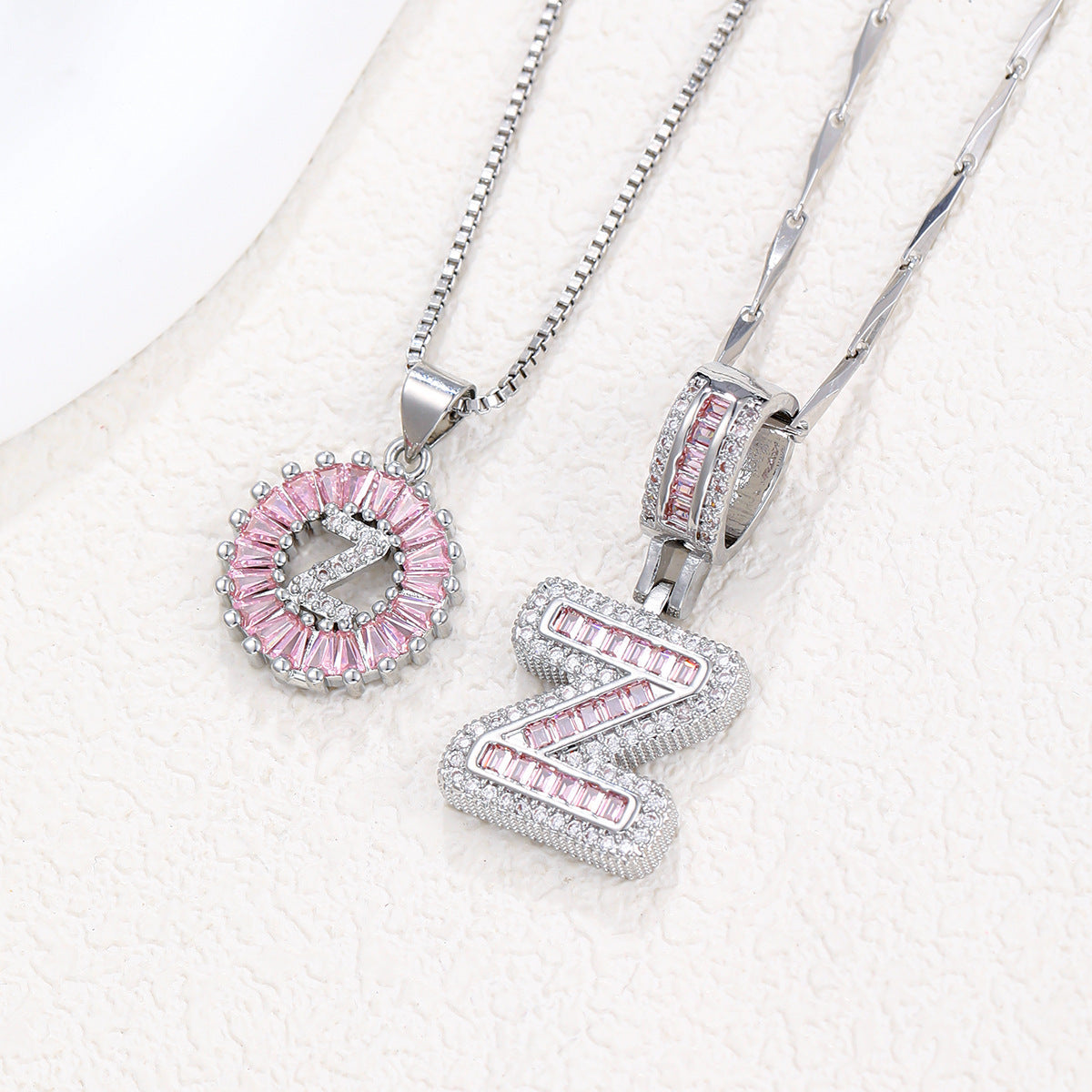 Silver-tone pendant necklace set with pink zircon rosette pendant and angled block letter pendant.
