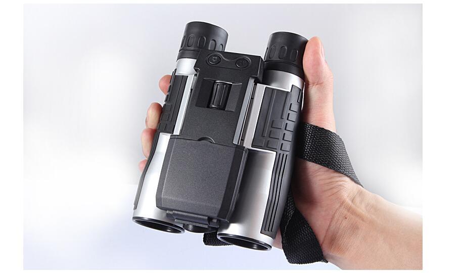 Hand holding a pair of black and silver binoculars with a strap on a light gray background
