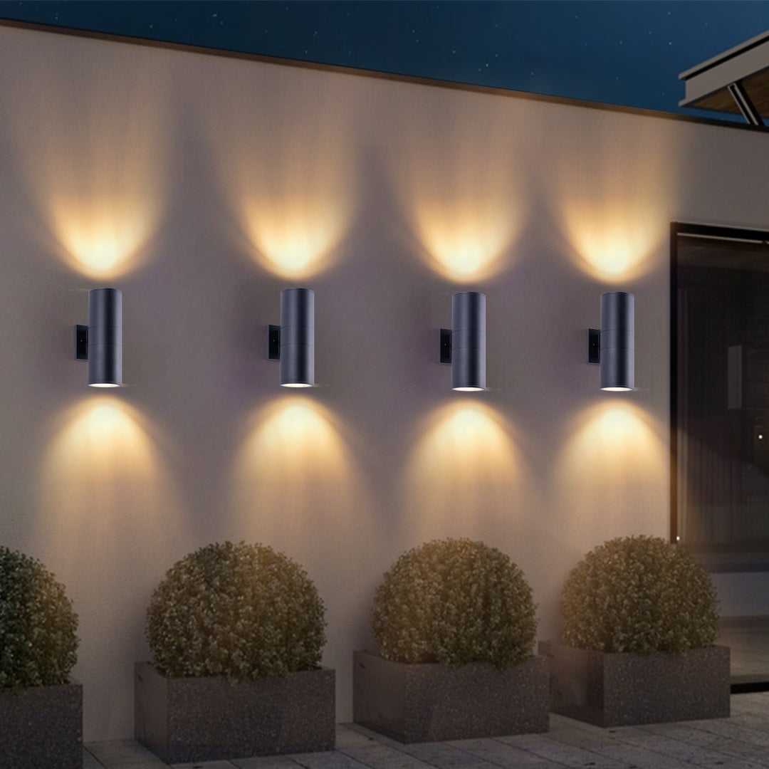 Set of four matte black cylindrical up-down outdoor wall lights with warm illumination.