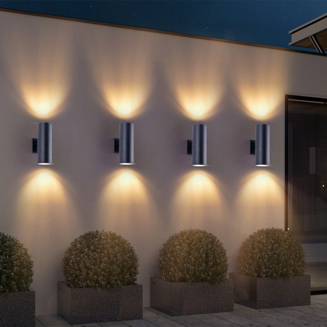 Matte black cylinder outdoor wall lights with warm up-down illumination along patio wall