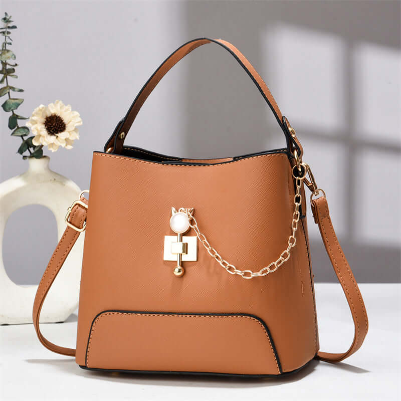 Rust brown PU leather bucket bag with top handle, shoulder strap, and gold chain charm