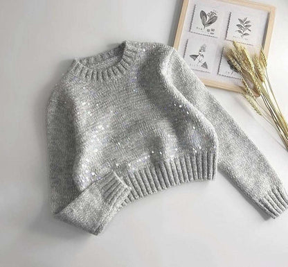 Silver sequin sweater on a light gray surface with decorative elements in the background