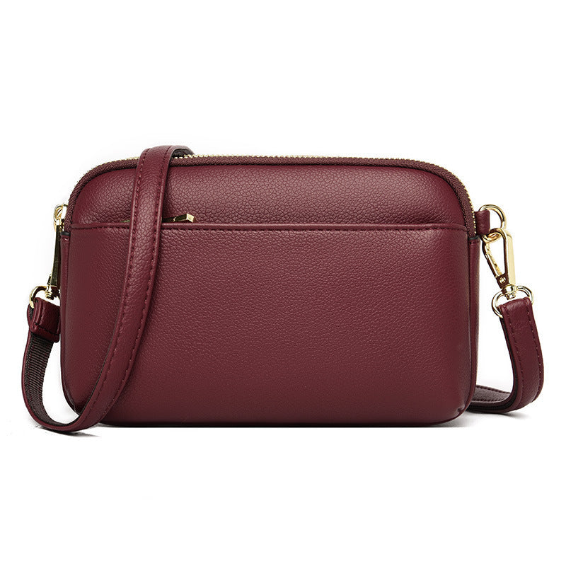 Wine red crossbody bag with curved front and gold zipper closure.
