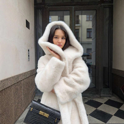 Woman wearing a white fur coat standing on a city street.