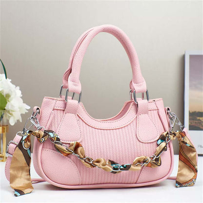 Pink braided chain crossbody handbag with top handles and front flap panels.