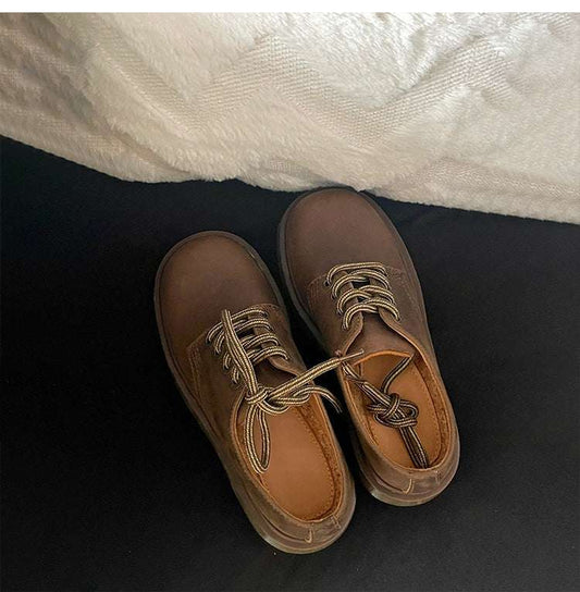 Pair of brown leather shoes with laces on a dark surface.