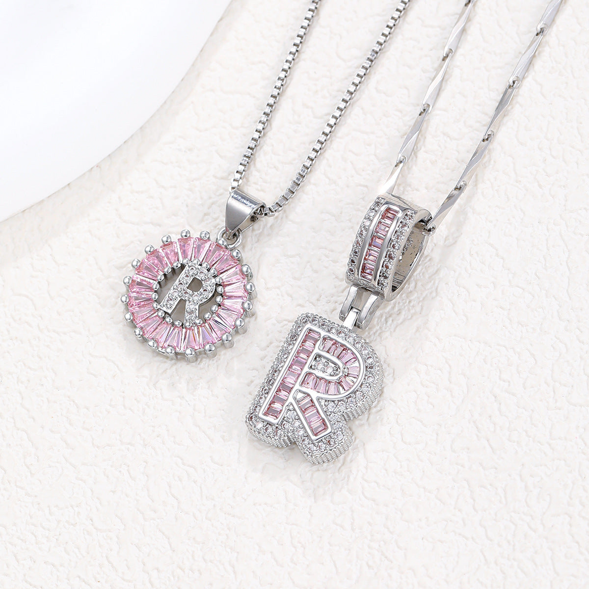 Silver-tone pendant necklace set with pink zircon rosette pendant and arched block letter pendant.