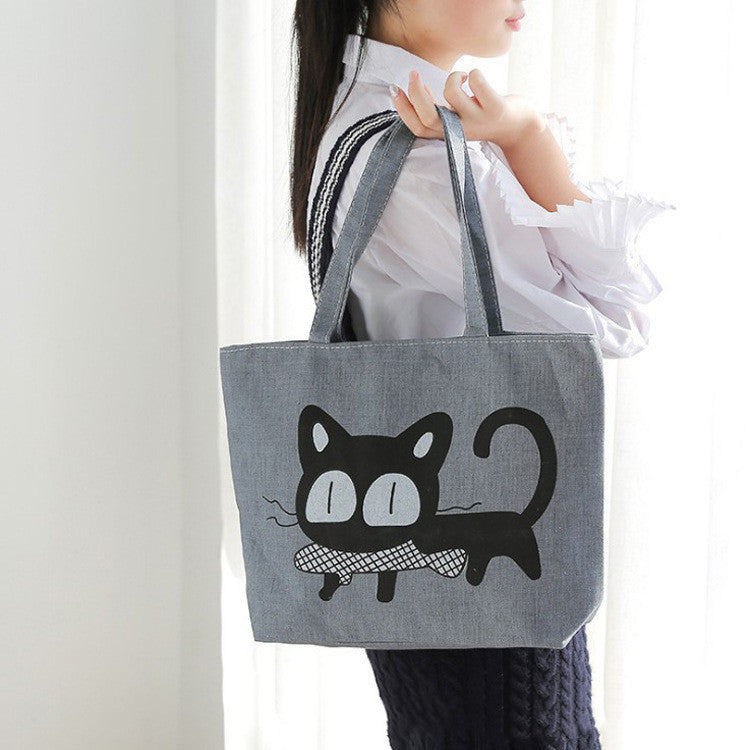 Gray canvas tote bag with large black cat face and whiskers graphic, top handles