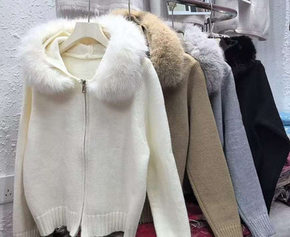 White sweater with fur hood on a hanger against a white wall.