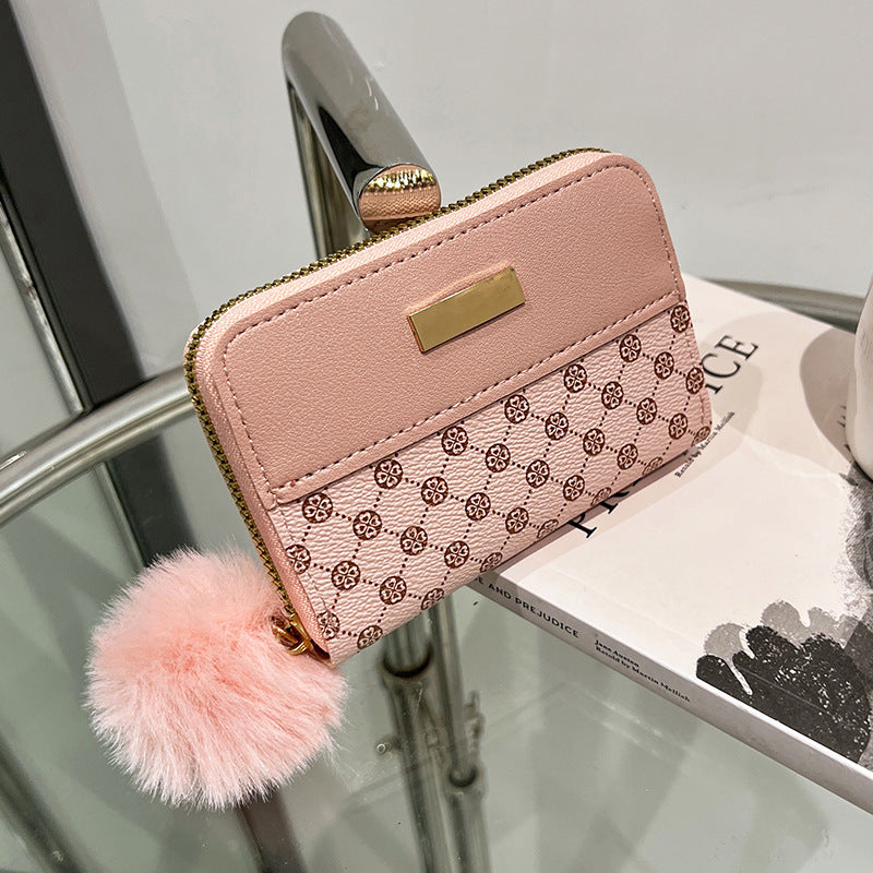 Pink patterned short wallet with gold clasp and fuzzy pom-pom detail