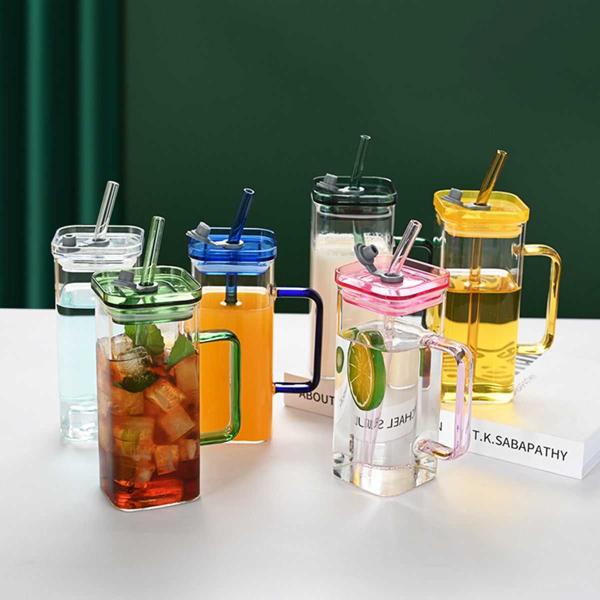 Assorted square glass cups with lids and straws in green, blue, yellow, and pink