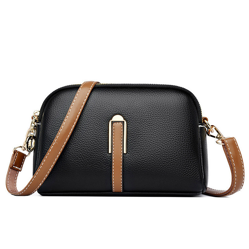 Black textured shoulder bag with zip top, tan strap detail, and chain crossbody
