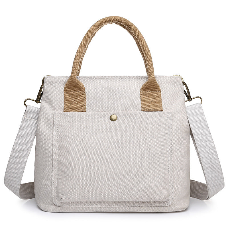 White canvas handbag with beige handle accents, front pocket, and crossbody straps