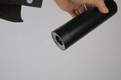 Black rechargeable electric pepper grinder tilted in hand, showing bottom and grinding head