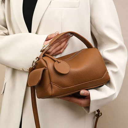 Dark brown leather pillow bag with front flap, top handle, and adjustable crossbody strap