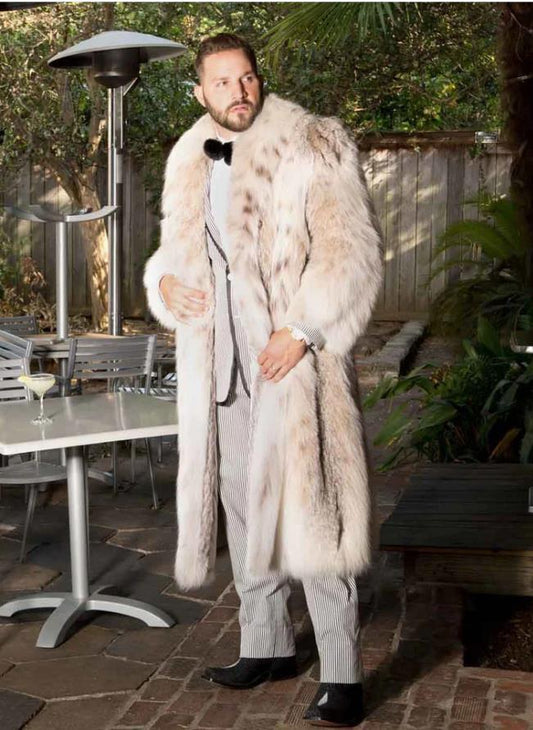 Man wearing a long fur coat standing outdoors near a patio table.