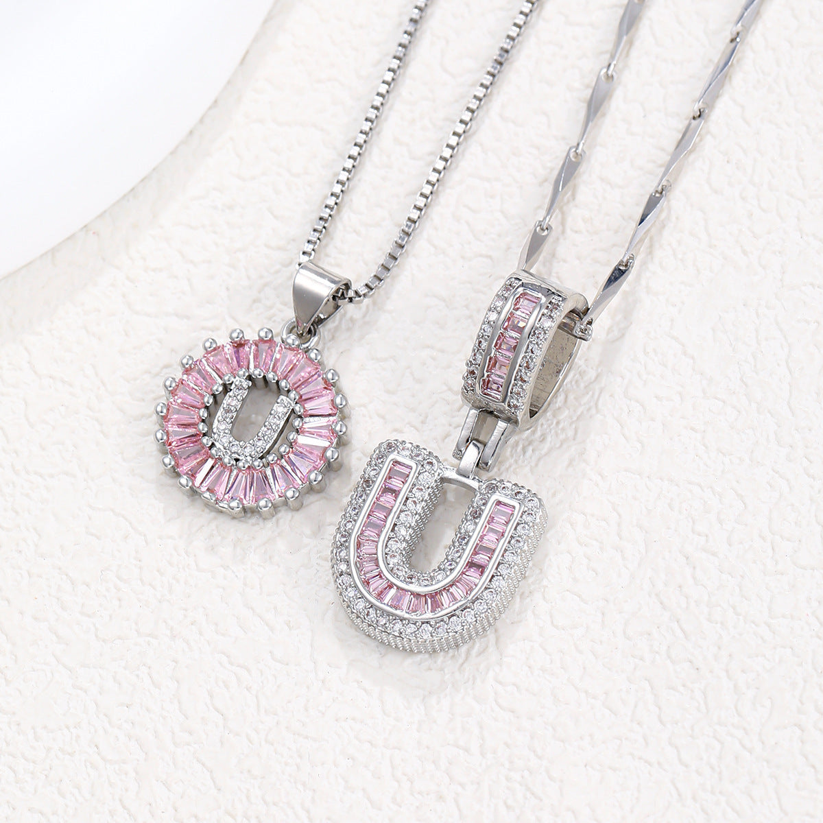 Silver-tone pendant necklace set with pink zircon rosette pendant and rounded block letter pendant.
