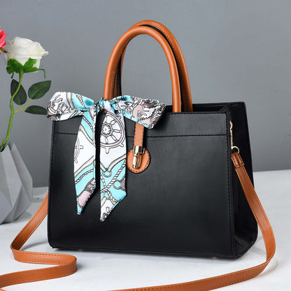 Large black crossbody tote with brown handles, blue patterned ribbon scarf, and metal clasp