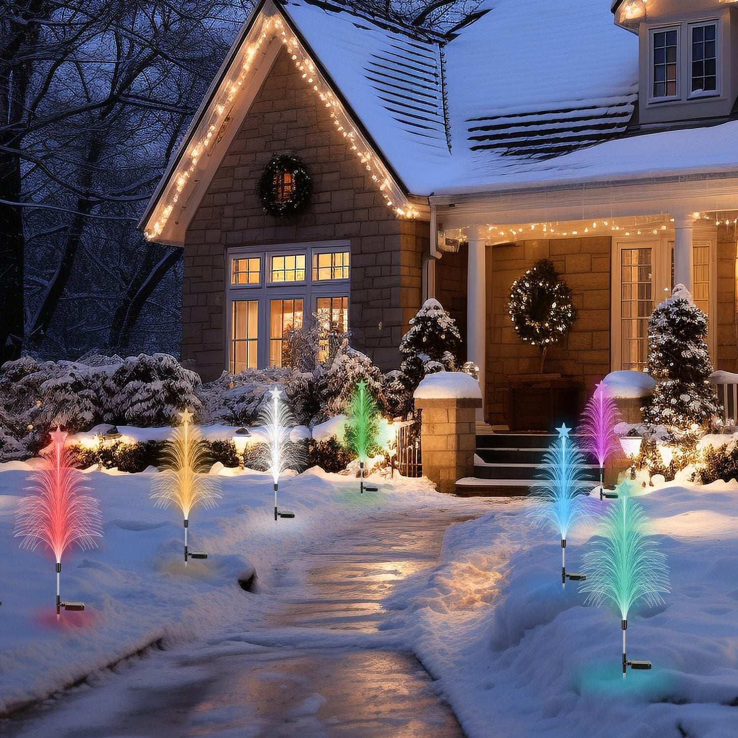 Decorative outdoor lights on a snowy pathway leading to a house with Christmas wreaths.