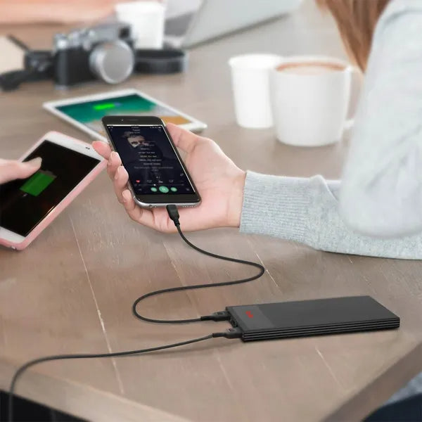 Black ultra-thin power bank charging a smartphone with connected cables in hand.