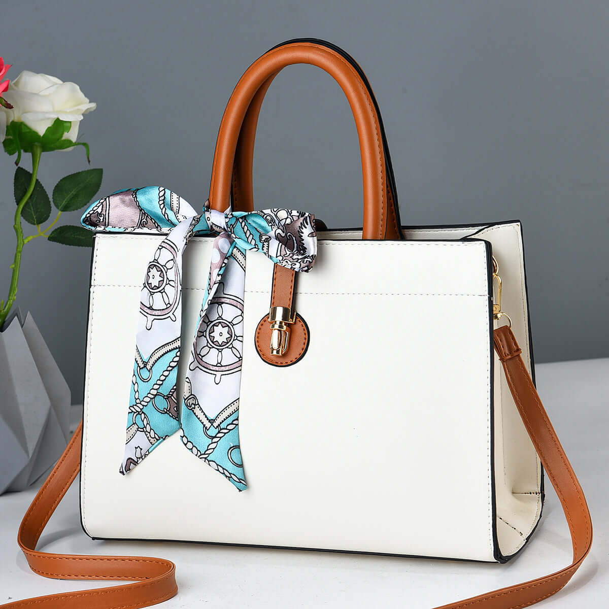 Large white crossbody tote with brown handles, blue patterned ribbon scarf, and metal clasp