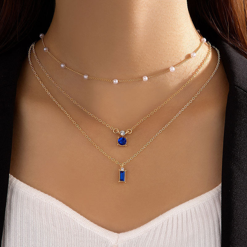 Multilayer pearl necklace with gold chain, white pearls, and blue round and bar pendants