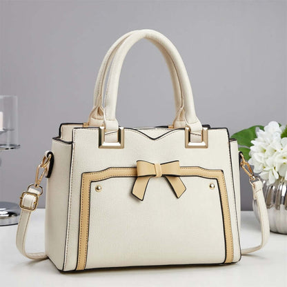 Cream commuting shoulder bag with bow front, gold hardware, and side crossbody strap