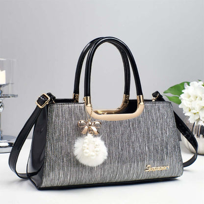 Structured glitter tote handbag in silver-gray with black handles and white pom-pom charm