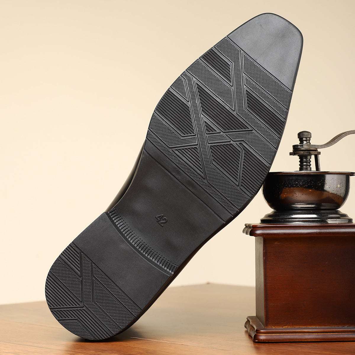 Black shoe sole with tread pattern next to a wooden coffee grinder on a beige background