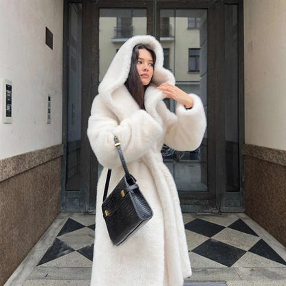 Woman in a white fur coat holding a black handbag on a city street.