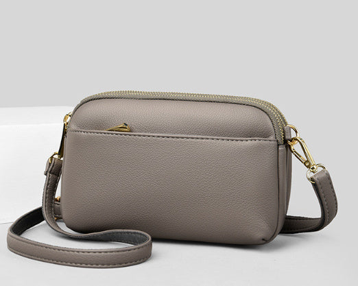 Light beige crossbody bag with gold zipper and adjustable shoulder strap.