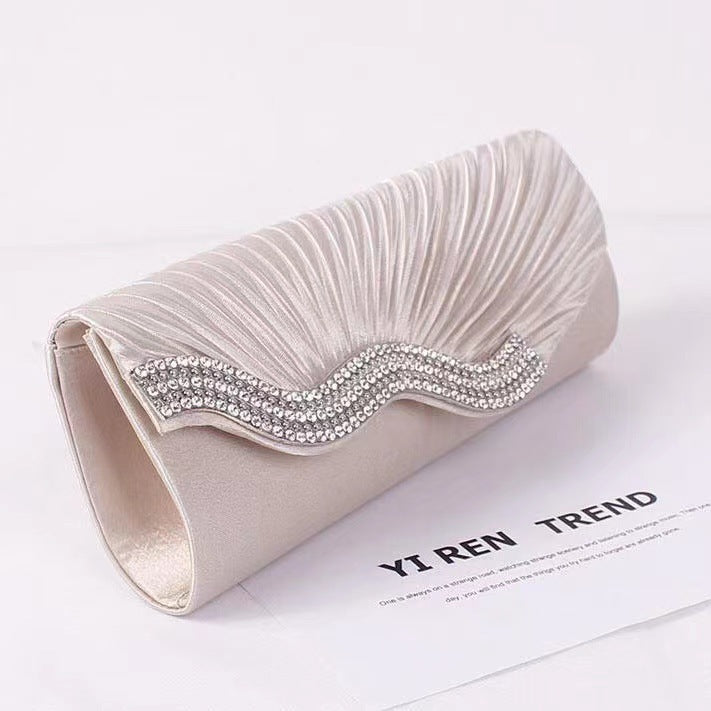 White satin clutch bag with textured ruching and rhinestone wave frame